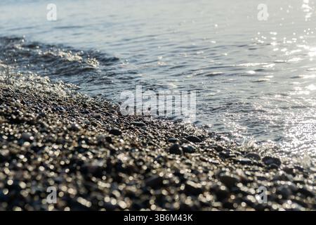 Sanfte Wellen, die sich bei Sonnenlicht am Morgen über glatte Kieselsteine am Strand waschen Stockfoto