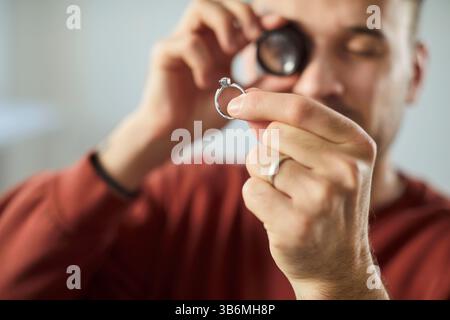 Ein Juwelier, der durch die Lupe schaut und den Goldring mit Diamant untersucht Stockfoto