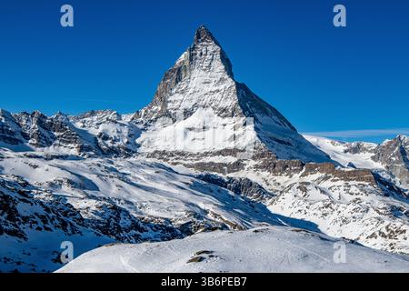 Das berühmte Matterhorn erhebt sich majestätisch über den verschneiten Alpen, dessen scharfer Gipfel sich in den blauen Himmel zieht – eine atemberaubende Winterszene Stockfoto