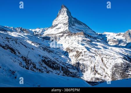 Das berühmte Matterhorn erhebt sich majestätisch über den verschneiten Alpen, dessen scharfer Gipfel sich in den blauen Himmel zieht – eine atemberaubende Winterszene Stockfoto