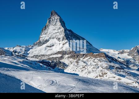 Das berühmte Matterhorn erhebt sich majestätisch über den verschneiten Alpen, dessen scharfer Gipfel sich in den blauen Himmel zieht – eine atemberaubende Winterszene Stockfoto