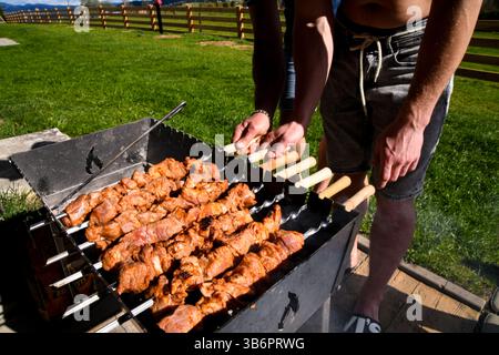 Zwei Männer, die Spieße mit Fleisch umdrehen, draußen grillen Stockfoto