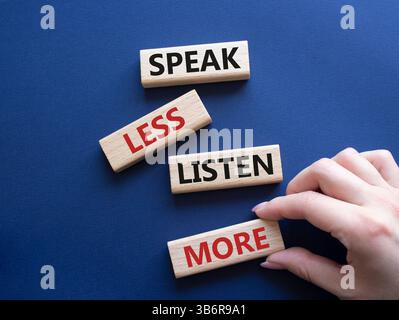Weniger sagen, mehr hören. Holzblöcke mit Wörtern sprechen weniger Hören Sie mehr. Wunderschöner tiefblauer Hintergrund. Geschäftsmann Hand. Geschäftlich und sprechen Sie l Stockfoto