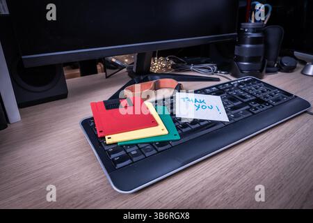 Vintage-Disketten, die auf der Computertastatur neben handgeschriebenen Notizen liegen und digitale Retro-Speicherspeicher hervorheben Stockfoto