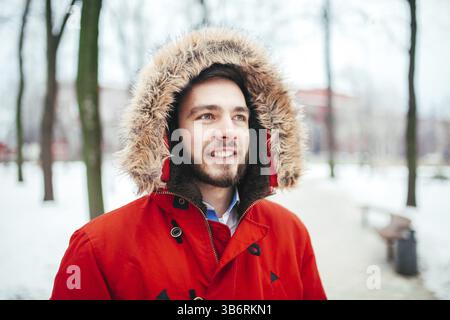 Porträt, Nahaufnahme eines jungen stilvoll gekleideter Mann lächelnd mit einem Bart im roten Winter Jacke mit Kapuze und Fell auf dem Kopf bekleidet. Winter und fr Stockfoto