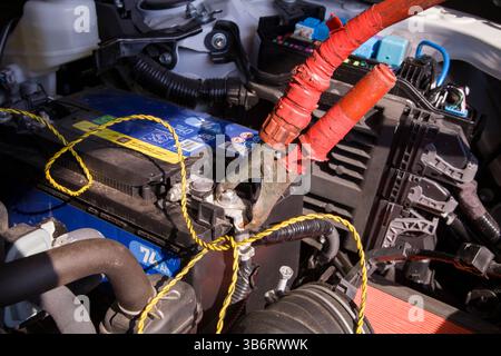 Eine sperrige rote Überbrückungskabelklemme, die mit dem Pluspol der Batterie verbunden ist und unter der geöffneten Motorhaube gut sichtbar ist Stockfoto