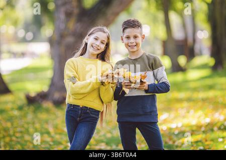 Glückliche Zwillinge Jugendliche Junge und Mädchen posiert umarmt sich im Herbst Park mit gefallenen gelben Blättern in der Hand bei sonnigem Wetter. Herbstthema Stockfoto