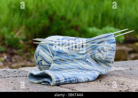 Hellblaues Sockengarn, das zum Stricken von Socken verwendet wird, mit Stricknadeln, die auf einer Steinoberfläche liegen Stockfoto