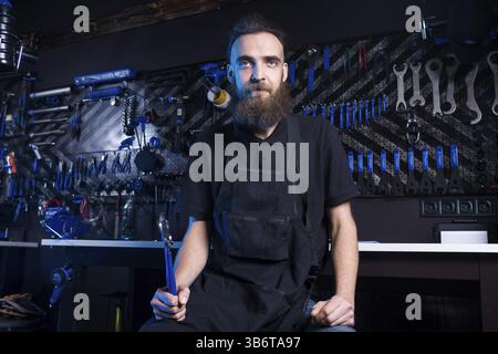 Portrait von Small Business Owner junger Mann mit Bart. Guy Fahrradmechaniker workshop Arbeiter sitzen mit Werkzeug in der Hand in einem schwarzen Kleide Stockfoto