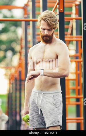 Sportmann, der auf die Uhr blickt, Steet Gym. Junge Muskelsportler, die nach einem guten Workout-Training Sportergebnisse auf Smart Watch überprüfen. Mann nach W Stockfoto