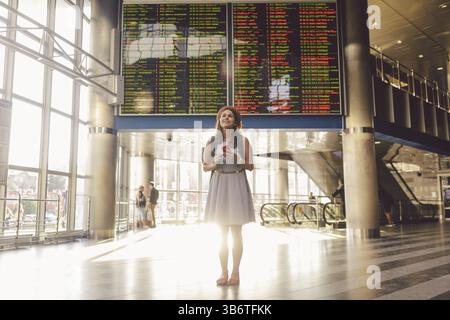 Thema Reisen und tranosport. Schönen jungen kaukasischen Frau in Kleid und Rucksack im Bahnhof oder Terminal auf einen Zeitplan fei Stockfoto