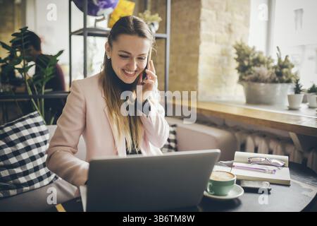 Glückliche Geschäftsfrau, Die Am Telefon Spricht. Frau im Café, Handy benutzen, mit Laptop arbeiten. Dame in der Cafeteria mit Telefon und Laptop, trinken Sie Tasse Kaffee Stockfoto