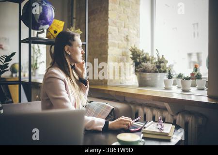 Glückliche Geschäftsfrau, Die Am Telefon Spricht. Frau im Café, Handy benutzen, mit Laptop arbeiten. Dame in der Cafeteria mit Telefon und Laptop, trinken Sie Tasse Kaffee Stockfoto