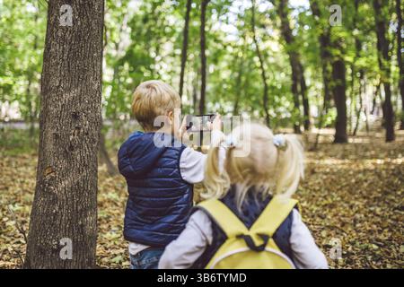 Kinder im Vorschulalter kaukasischen Bruder und Schwester Bilder von einander auf Handy Kamera in Forest Park Herbst. Thema der Hobby- und Aktiv Stockfoto