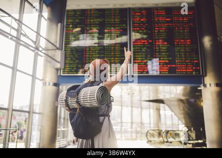 Thema Reisen mit den öffentlichen Verkehrsmitteln. junge Frau zurück in kleid und hut hinter Rucksack Camping Ausrüstung für Schlafsack, Isoliermatte sieht schedul Stockfoto