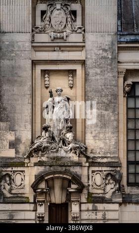 Eine detaillierte Steinskulptur auf einer Gebäudefassade, die eine zentrale Figur darstellt, die von kleineren Figuren umgeben ist. Die Architektur verfügt über ein klassisches Element Stockfoto