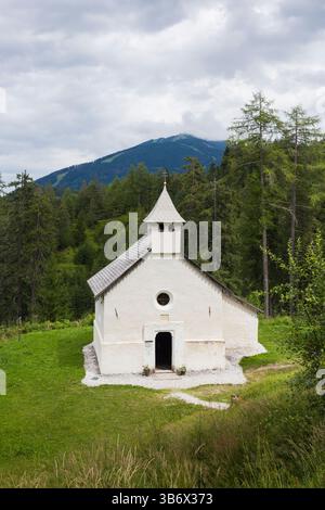 Capella di San Salvatore, San Candido, Dolomiten, Italien, typische alte alpenländische, weiß getünchte Steinkirche in den Bergen und im Wald. Stockfoto