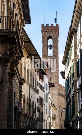 Eine enge Straße in Florenz, Italien, mit historischer Architektur und einem hohen Glockenturm im Hintergrund. Die Gebäude sind mit kunstvollen Details versehen Stockfoto