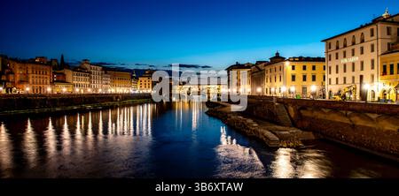Ein ruhiger Blick auf einen Fluss in der Abenddämmerung mit Stadtgebäuden, die entlang der Ufer beleuchtet sind. Der Himmel wechselt von blau zu dunkel und reflektiert auf dem Wasser Stockfoto
