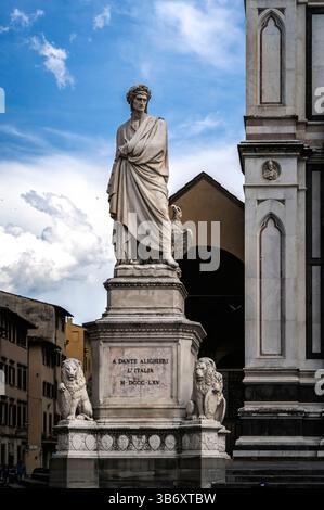 Eine Marmorstatue von Dante Alighieri steht an einem öffentlichen Platz, umgeben von architektonischen Elementen und Löwenskulpturen. Der Himmel ist teilweise Stockfoto