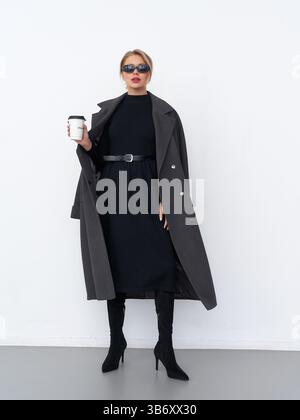 Schicke Frau in stilvoller Kleidung hält eine Kaffeetasse in einem Studio Stockfoto