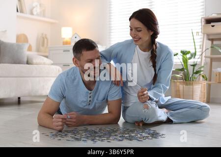 Glückliches Paar löst zusammen Puzzle auf dem Boden drinnen Stockfoto