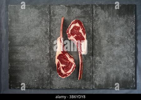 Rohe Tomahawk-Steaks auf dunkler Schieferoberfläche Stockfoto