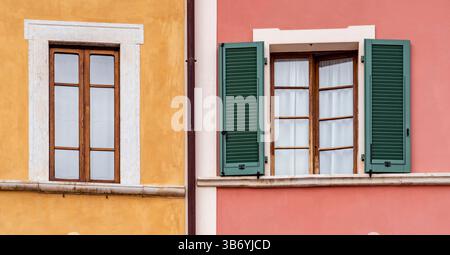 Zwei Fenster mit Holzrahmen und grünen Fensterläden an farbenfrohen Wänden, eines gelb und eines rosa, mit architektonischen Details und Kontrastfarben. Stockfoto