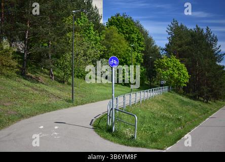 Ein Asphaltradweg führt durch einen Stadtpark zwischen Bäumen mit grünen Blättern. Ort für sportliche Erholung. Radweg für Radfahrer. Stockfoto