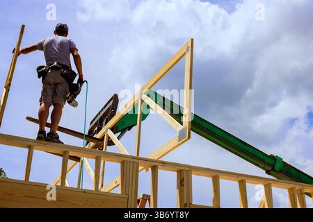 Der Arbeiter steht auf der Struktur, während er den Teleskopladerkran verwendet, um während des Arbeitstages Holzbalken in Position zu bringen Stockfoto