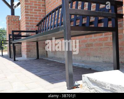 Schwarze Metallbänke mit Lattensitzen und Rückenlehnen, die an Ziegelsteinpflastern in der Nähe von roten Ziegeln in traditionellem Mauerwerk verankert sind, mit einem Blick aus der Nähe von Th Stockfoto