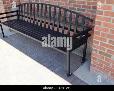 Schwarze Metallbänke mit Lattensitzen und Rückenlehnen, die an Ziegelsteinpflastern in der Nähe von roten Ziegeln in traditionellem Mauerwerk verankert sind, mit einem Blick aus der Nähe von Th Stockfoto