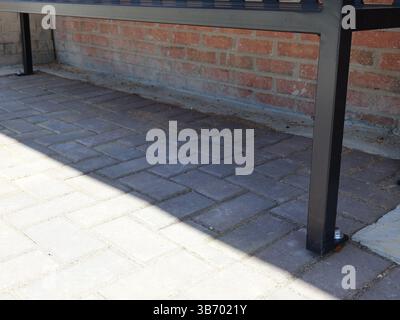 Schwarze Metallbänke mit Lattensitzen und Rückenlehnen, die an Ziegelsteinpflastern in der Nähe von roten Ziegeln in traditionellem Mauerwerk verankert sind, mit einem Blick aus der Nähe von Th Stockfoto