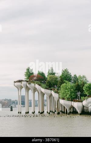 Urbane Parkstruktur, die sich über dem Wasser erhebt, umgeben von üppigem Grün an einem ruhigen Tag mit bewölktem Himmel. Stockfoto
