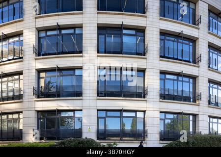 Blick auf die Straße auf ein großes, geschwungenes modernes Bürogebäude mit Steinverkleidung und Fensterreihen. Stockfoto