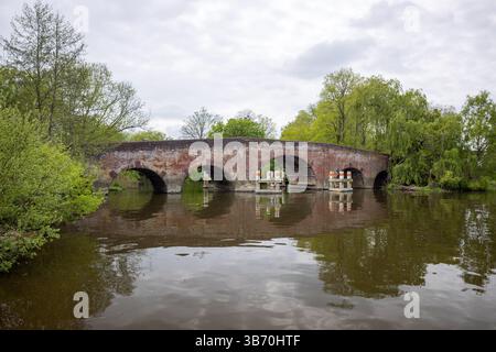 Historische mehrbogige rote Backsteinbrücke, die einen Fluss überspannt und von üppigen Bäumen umgeben ist. Stockfoto