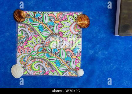 Ein farbenfroher, handgezeichneter Mandala ist mit Muscheln auf einem leuchtend blauen Hintergrund verziert Stockfoto
