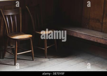 Zwei antike Holzstühle und alte Bank in gemütlichem rustikalem Interieur mit sanftem Licht. Stockfoto
