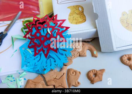 Ungebackene Puzzleteile aus Ton und bunte Papierausschnitte sind auf einem Tisch in einer Handwerkstatt verstreut Stockfoto