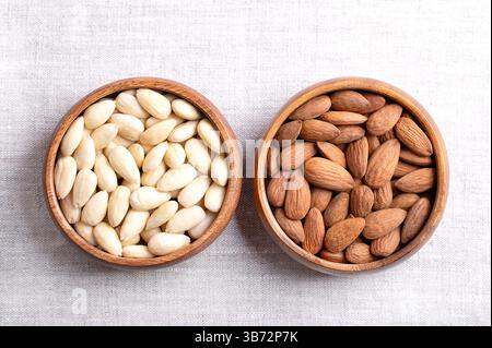 Mandeln mit Haut und hautlose Mandeln in Holzschalen auf Leinen. Früchte von Prunus amygdalus, syn. Prunus dulcis, mit Samenmänteln und blanchiert. Stockfoto