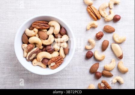 Geröstete Nüsse, knusprige Nussmischung, schnelle Snacks in einer weißen Schüssel auf Leinen. Mischung aus gerösteten Cashewkernen, Mandeln, Haselnüssen, Paranüssen und Pekannüssen. Stockfoto