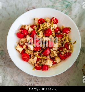 Knuspriger griechischer Salat aus Kirschtomaten, Fetakäsewürfeln, Gurkenbändern und roten Zwiebeln in Oregano-Öl Stockfoto