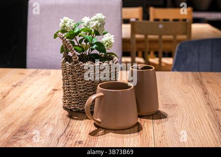 Weiße Hortensie in einem Korb mit einer Tasse und einem Milchkännchen auf dem Tisch Stockfoto