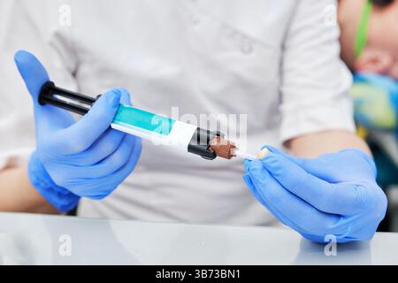 Zahnarzt in Blue Handschuhen Zement für Zahnkrone vorbereiten. Detaillierte Ansicht mit den Werkzeugen und dem Klebstoff, das zum Befestigen von Zahnkronen verwendet wird. I Stockfoto