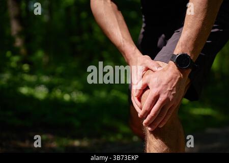 Läufer, der das Knie schmerzt während des Workouts im Sommerpark. Der Mann hat beim Laufen Verletzungen. Männlicher Sportler mit Knieschmerzen nach Sportübungen Stockfoto