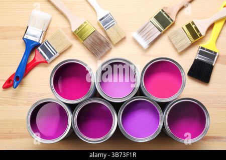 Dosen mit Farbe in Violett und Pinsel auf hölzernem Hintergrund, Draufsicht Stockfoto
