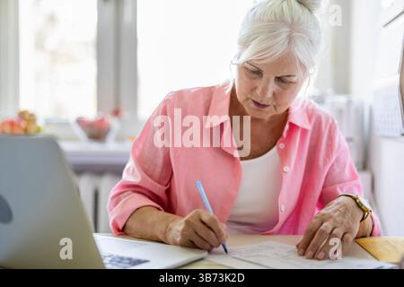 Senior Frau, die zu Hause Finanzberichte ausfüllt Stockfoto