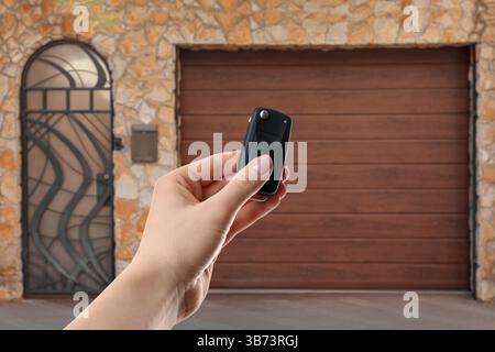 Frau, die das elektrische Tor im Freien mit Fernbedienung steuert, Nahaufnahme Stockfoto