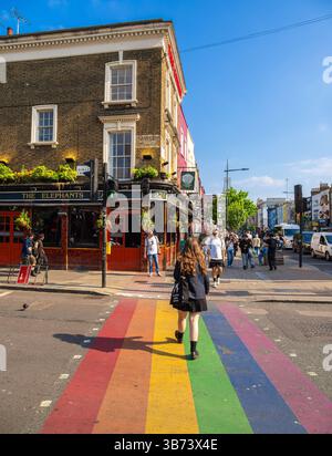 London, Großbritannien - 28. April 2025: Eine Person spaziert über einen regenbogenfarbenen Quersteg in einem lebhaften Stadtteil von Camden Town mit einem Pub und Plätzen Stockfoto