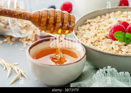 Honig tropft aus hölzernem Honiglöffel. Haferbrei im Hintergrund. Stockfoto